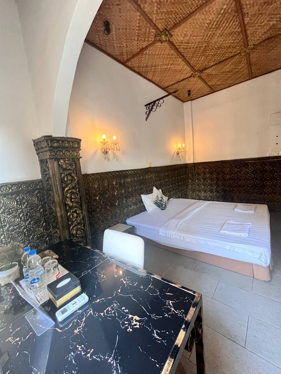 A room with a bed, a small table with toiletries, and a decorative pillar.