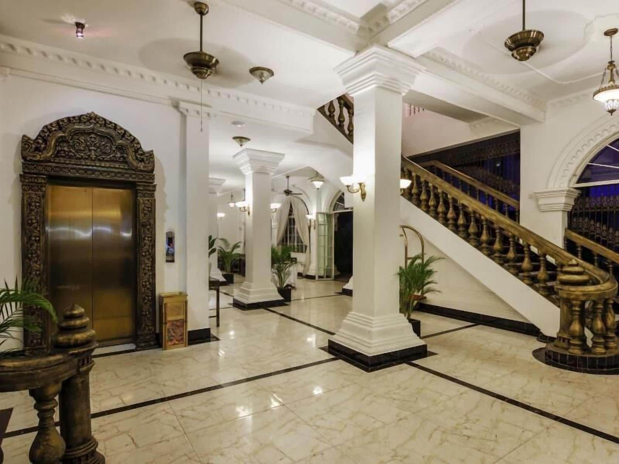 Een statige lobby met een marmeren vloer, een centrale trap en een grote, versierde lift.
