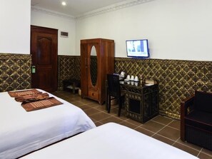 Una habitación de hotel con dos camas, un armario de madera, un escritorio con silla y un televisor en la pared.