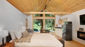 A bedroom with a large bed, wooden ceiling, a dining area with a table and chairs, a kitchen with a refrigerator and microwave, and a fireplace. - Creekside Maroon Bells Cabin at T-Lazy-7 Ranch, 5 Min to Maroon Bells & Highlands, 10 to Aspen (Aspen)