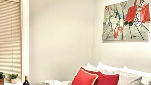 A bedroom with a bed, a painting, a bottle of wine, and a tray with food.