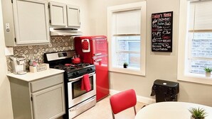 A kitchen with a red refrigerator, a stove, and a coffee station. There is a chalkboard menu on the wall listing today's menu items.
