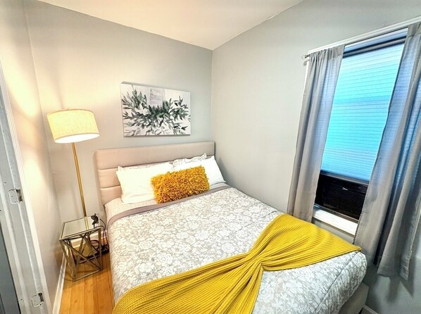 A bedroom with a bed, a bedside lamp, a window with curtains, and a wall-mounted artwork. - Wicker Park by Downtown and Salt Shed Special 159.00 Oct 12-16, 169.00 Oct 25-30 (Chicago)