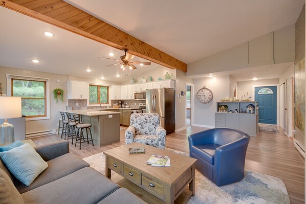 A spacious living area with a sofa, coffee table, and a blue armchair. A kitchen with white cabinets and a refrigerator is visible in the background. - Lakefront Osceola Vacation Rental - Dogs Welcome! (Osceola)