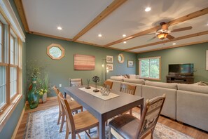 A dining area with a wooden table, chairs, and a vase with flowers. There is a sofa and a television in the background. - Lakefront Osceola Vacation Rental - Dogs Welcome! (Osceola)