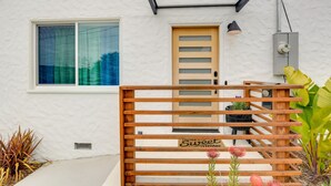 A modern house with a wooden gate, a white exterior, a window with curtains, and a door with a light fixture above it. - Pet-Friendly El Cerrito Home: Deck, Sauna & Views! (El Cerrito)