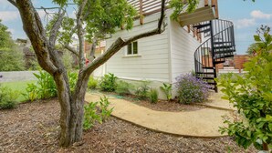 A residential building with a spiral staircase, a tree in the foreground, and a garden with various plants. - Pet-Friendly El Cerrito Home: Deck, Sauna & Views! (El Cerrito)