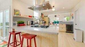 A modern kitchen with a central island, red bar stools, and a large window providing natural light. - Pet-Friendly El Cerrito Home: Deck, Sauna & Views! (El Cerrito)