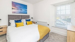 Et moderne soveværelse med en stor seng, en grå sengegavl og et vindue med persienner.