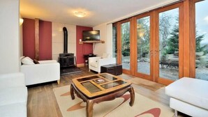 Een moderne woonkamer met een salontafel met glazen blad, witte banken, een open haard en grote schuifdeuren naar een tuin.