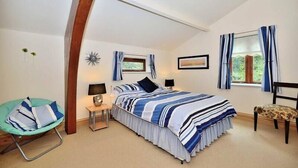 Een slaapkamer met een bed, een stoel, een nachtkastje, een lamp en een raam met gordijnen.