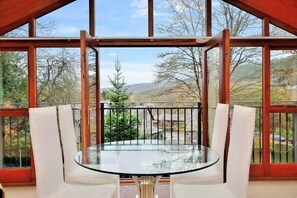 A glass table with white chairs in a room with large windows and a balcony. - Betws Y Coed Holiday Home (Betws-Y-Coed)