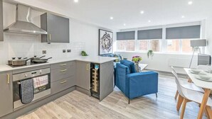 A modern kitchen with grey cabinets, a built-in oven, and a dining area with a blue sofa and a white table.