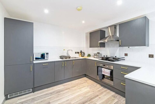 A modern kitchen with grey cabinets, a microwave, a stove, and a sink. - Charles House by Guestz (Preston)