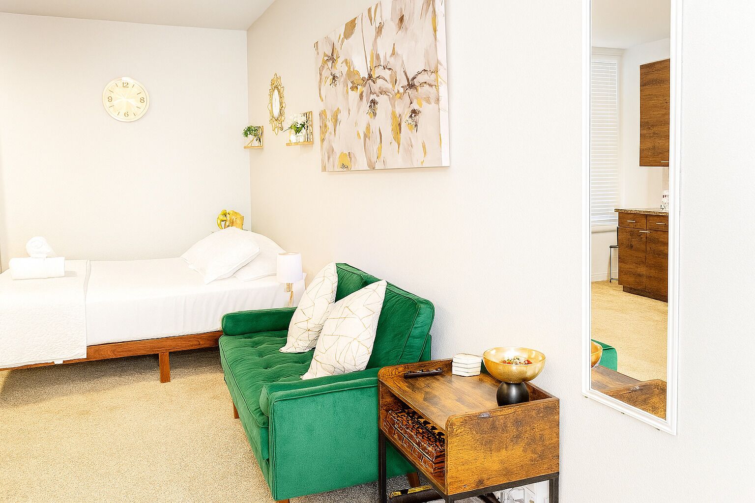 A hotel room with a bed, a green sofa, a small wooden table, and a wall clock.