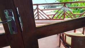 Una puerta de madera con un picaporte metálico, vista a una playa con barandilla de madera y una silla con cojín.