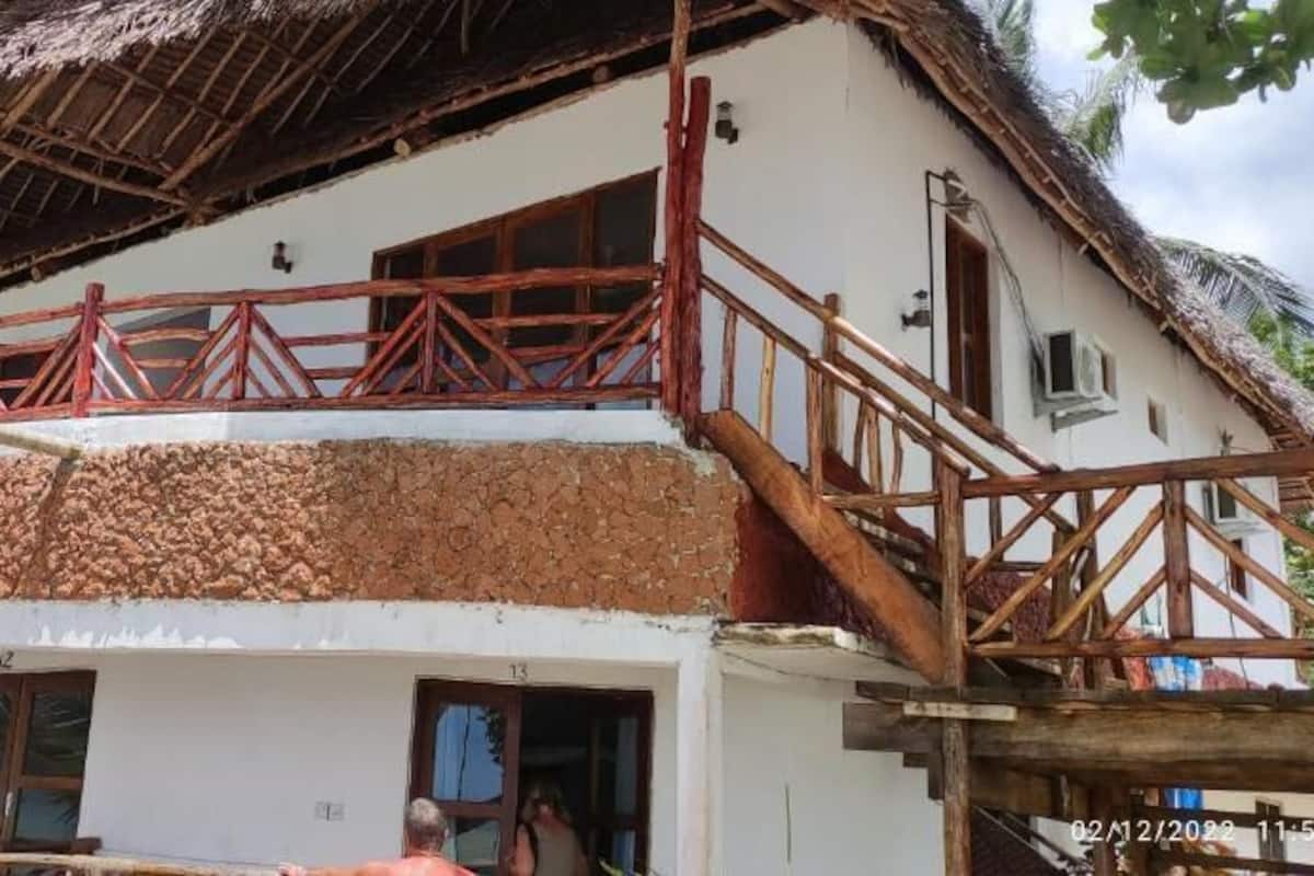 Un bâtiment à deux étages, doté d’un toit de chaume, d’un balcon avec une balustrade en bois et d’un escalier menant à l’étage supérieur.
