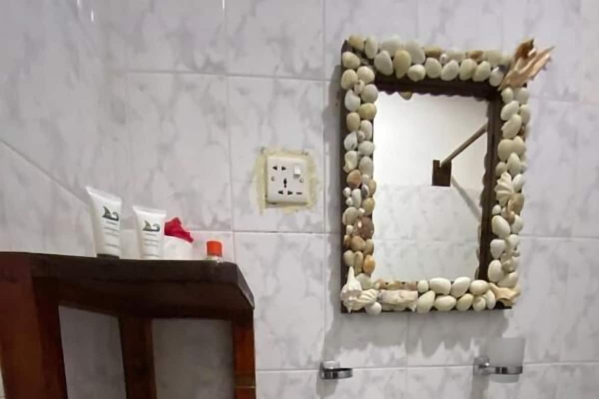 Une salle de bain avec une étagère en bois, un lavabo et un miroir encadré de pierres.