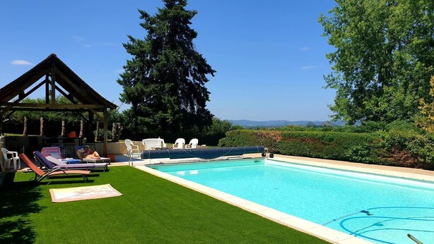 Une piscine bordée de gazon synthétique, dotée de chaises longues et d’une pergola.