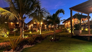Zona turística bien iluminada con palmeras, un edificio de techo de paja y un espacio de estar cubierto.
