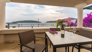Une terrasse avec une table dressée pour deux personnes, offrant une vue sur un plan d’eau et des collines.