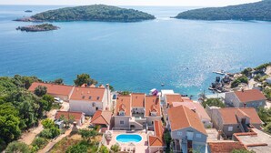 Un quartier résidentiel situé sur la côte, avec des maisons à étages, une piscine et une vue sur la mer et les îles.