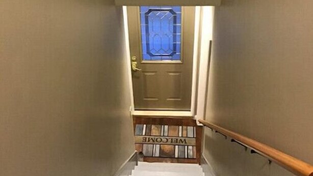 Uma escadaria leva a uma porta com um tapete de boas-vindas e uma janela com moldura azul acima.