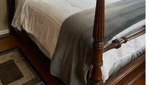 Uma cama de dossel com estrutura de madeira, roupa de cama branca e um quadro na parede acima.