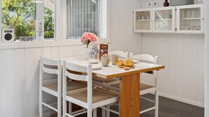 Una mesa de comedor blanca con sillas, un florero con flores rosadas, un cartón de leche y un plato con pasteles.