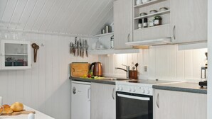 Una cocina con armarios blancos, una estufa, un fregadero y diversos utensilios.