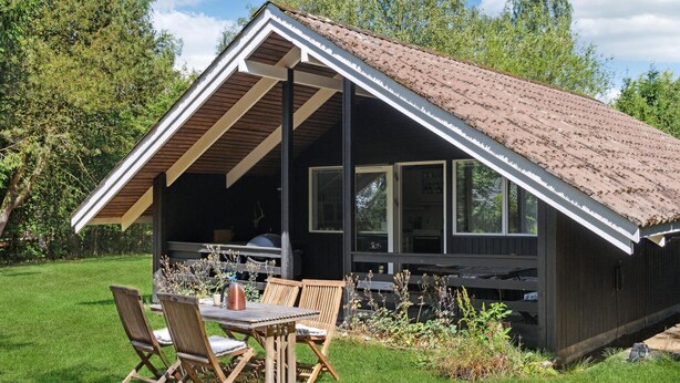 Una cabaña de madera con techo inclinado, un porche cubierto y una zona de comedor con mobiliario de exterior.