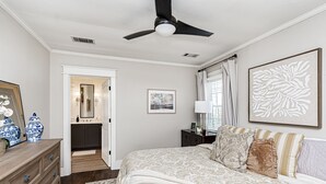 Un dormitorio con cama, cómoda, ventilador de techo, obras de arte y vista al baño.