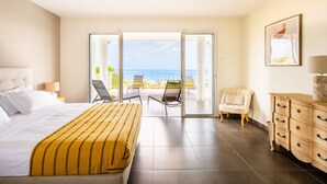 Ein Hotelzimmer mit Bett, Sofa, Sessel, Kommode und einem Balkon mit Meerblick.