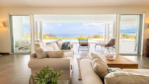 Ein geräumiges Wohnzimmer mit einer großen Schiebeglastür, die auf einen Balkon mit Pool und Meerblick führt.