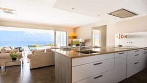 Eine moderne Küche mit einer großen Kochinsel, ein Essbereich mit Meerblick und ein Wohnzimmer mit Sofa und Couchtisch.