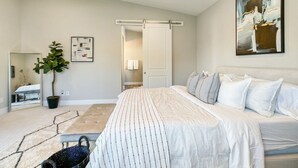 A bedroom with a bed, a potted plant, a painting, and a sliding door leading to another room.