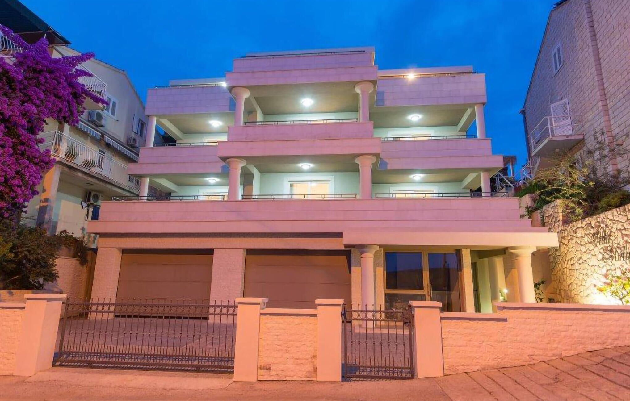 Un edificio de varios pisos con balcones, entrada protegida por un portón y camino de acceso.