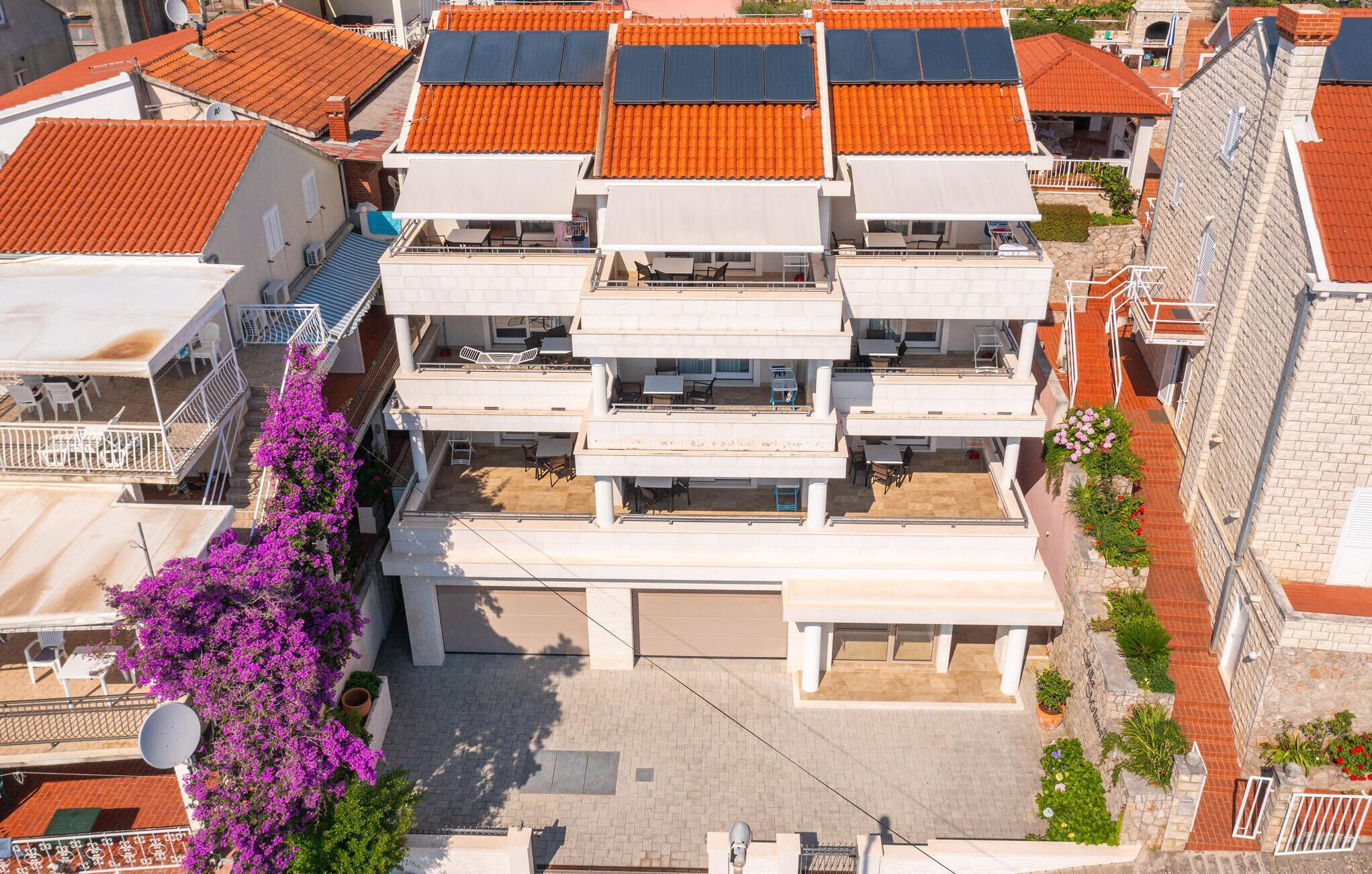 A multi-story building with balconies, solar panels, and a garden with purple flowers.