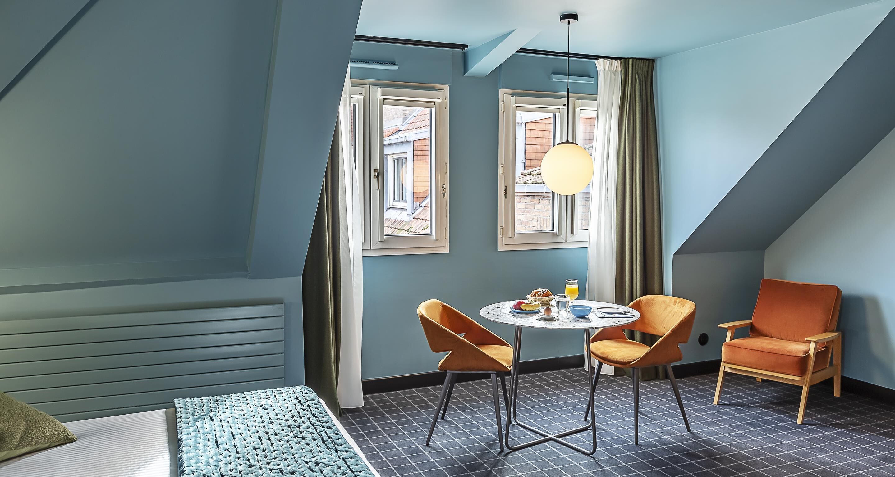 A room with a bed, two chairs, a table with breakfast, and a window with curtains.