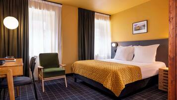 Ein Hotelzimmer mit Bett, Sessel, Schreibtisch und Lampe.