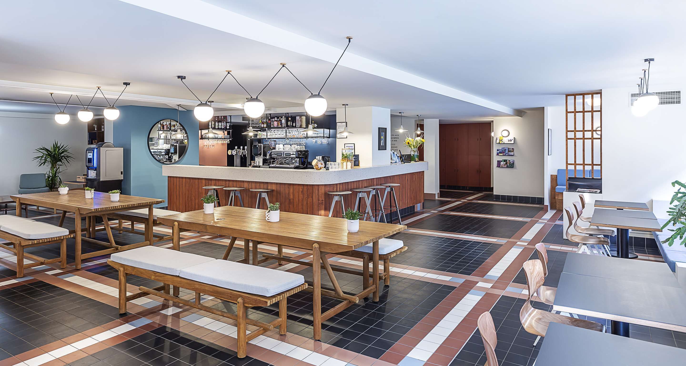 Un lobby moderno de hotel con una zona de bar central, mesas y bancos de madera, y un suelo estampado.