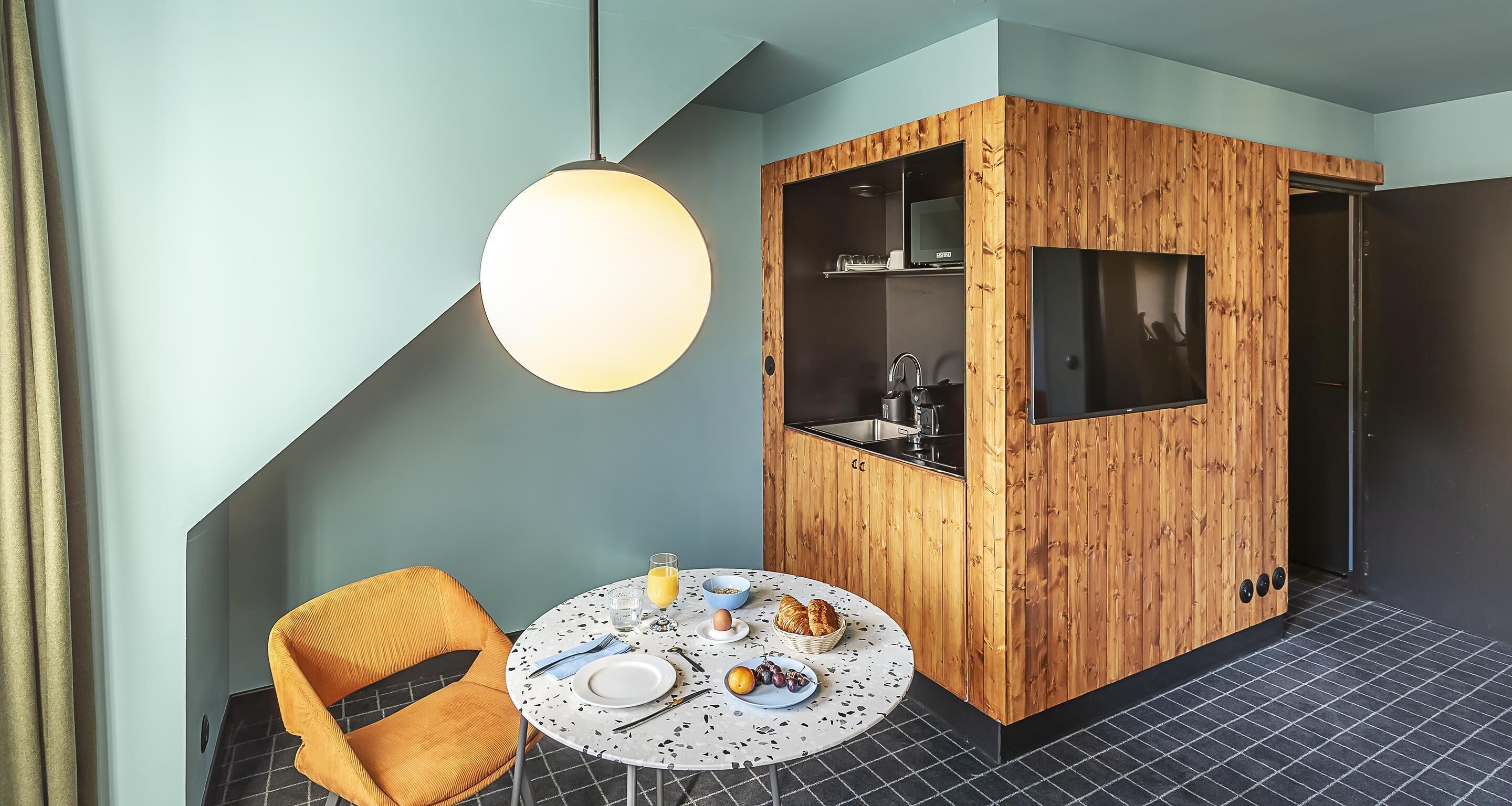 A modern room with a round table set for breakfast, a wooden cabinet with a TV, and a large pendant light.