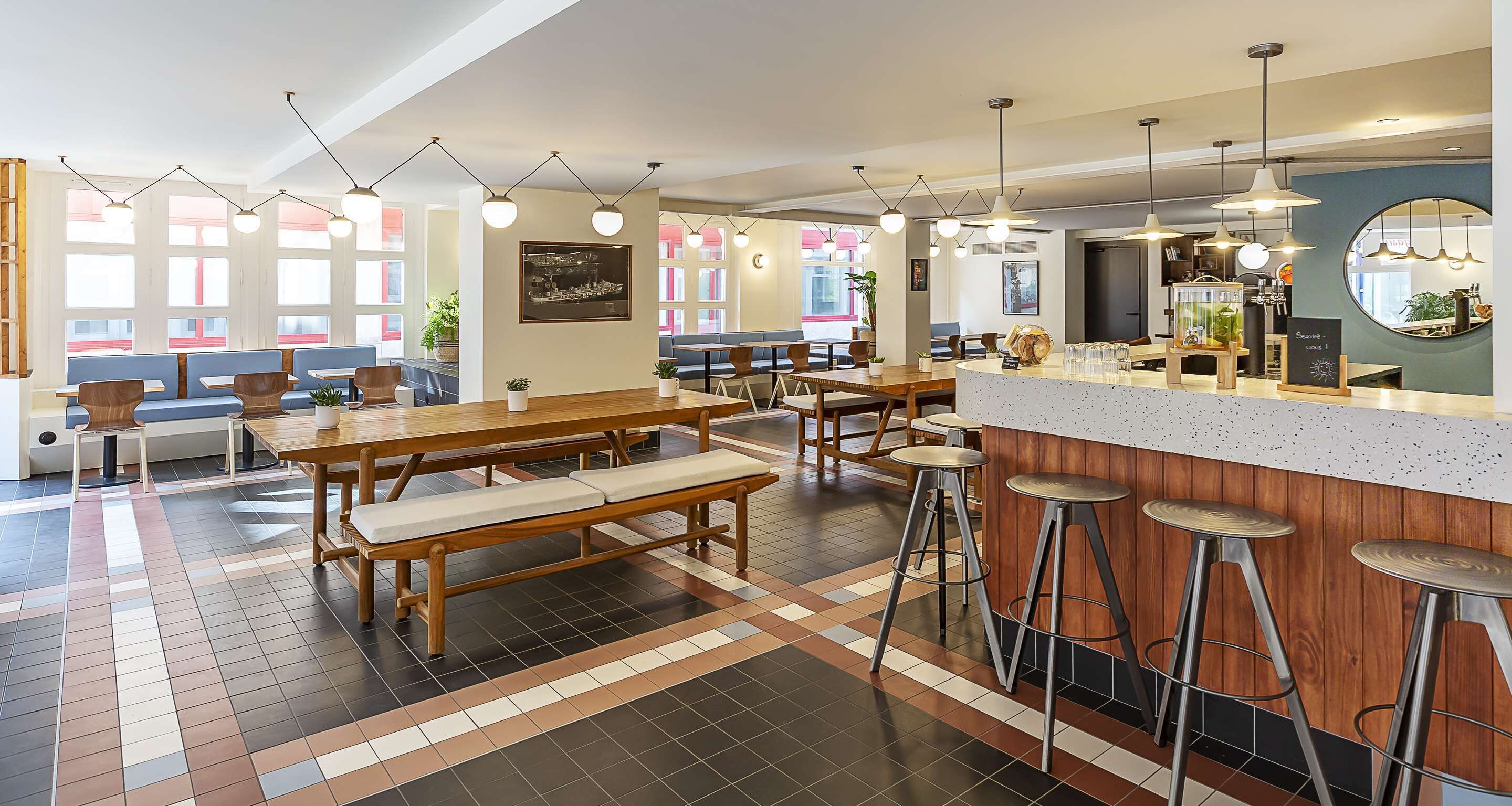 A modern restaurant with wooden tables and benches, bar stools, and pendant lighting.