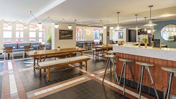 Un restaurante moderno con mesas y bancos de madera, taburetes de bar e iluminación colgante.