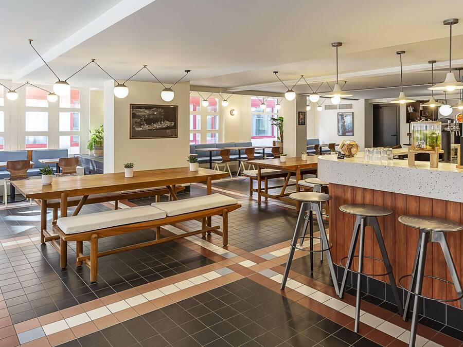 A modern restaurant with wooden tables and benches, bar stools, and pendant lighting.