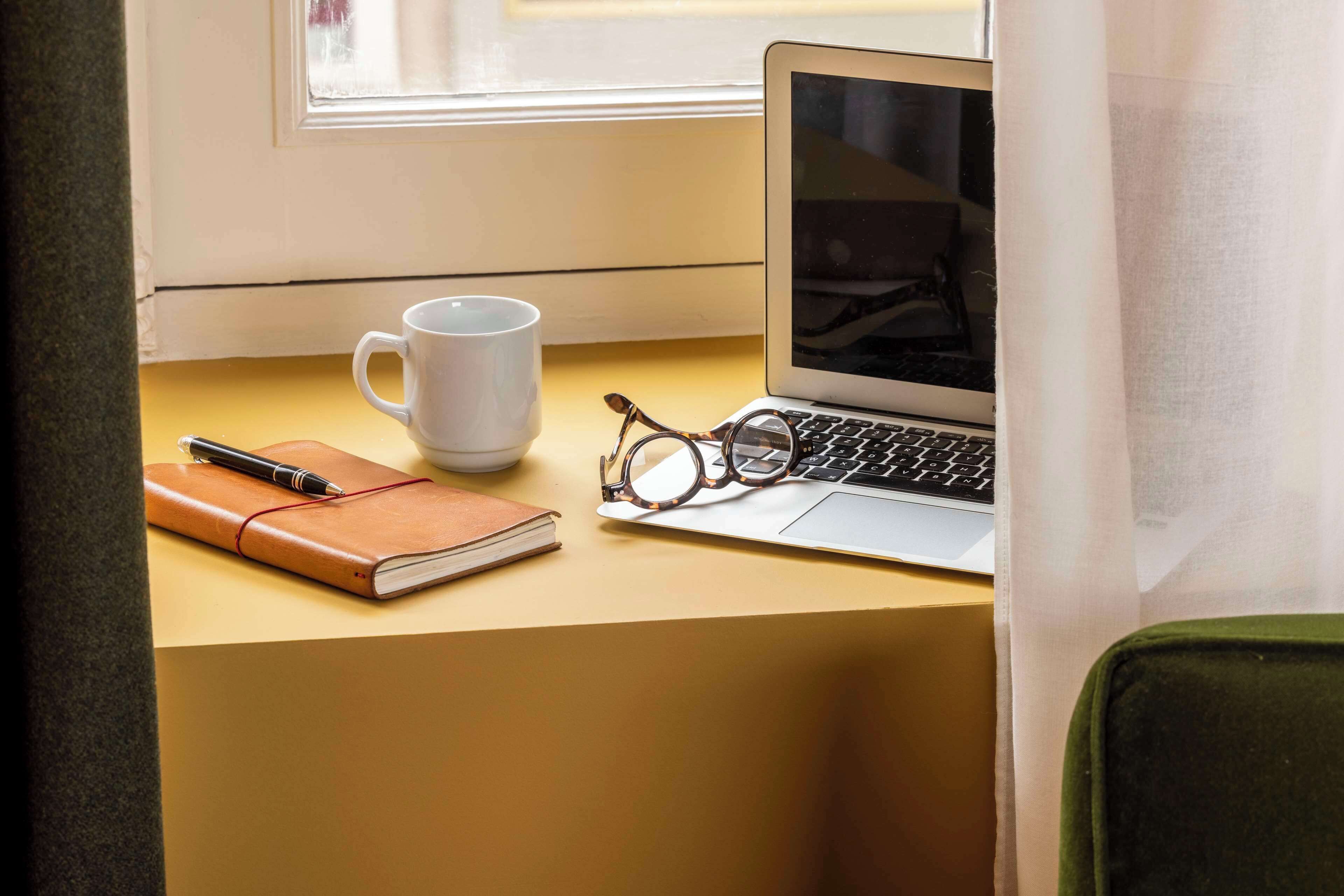 Un ordinateur portable est posé sur une table, accompagné d’un carnet, d’un stylo, de lunettes et d’une tasse.