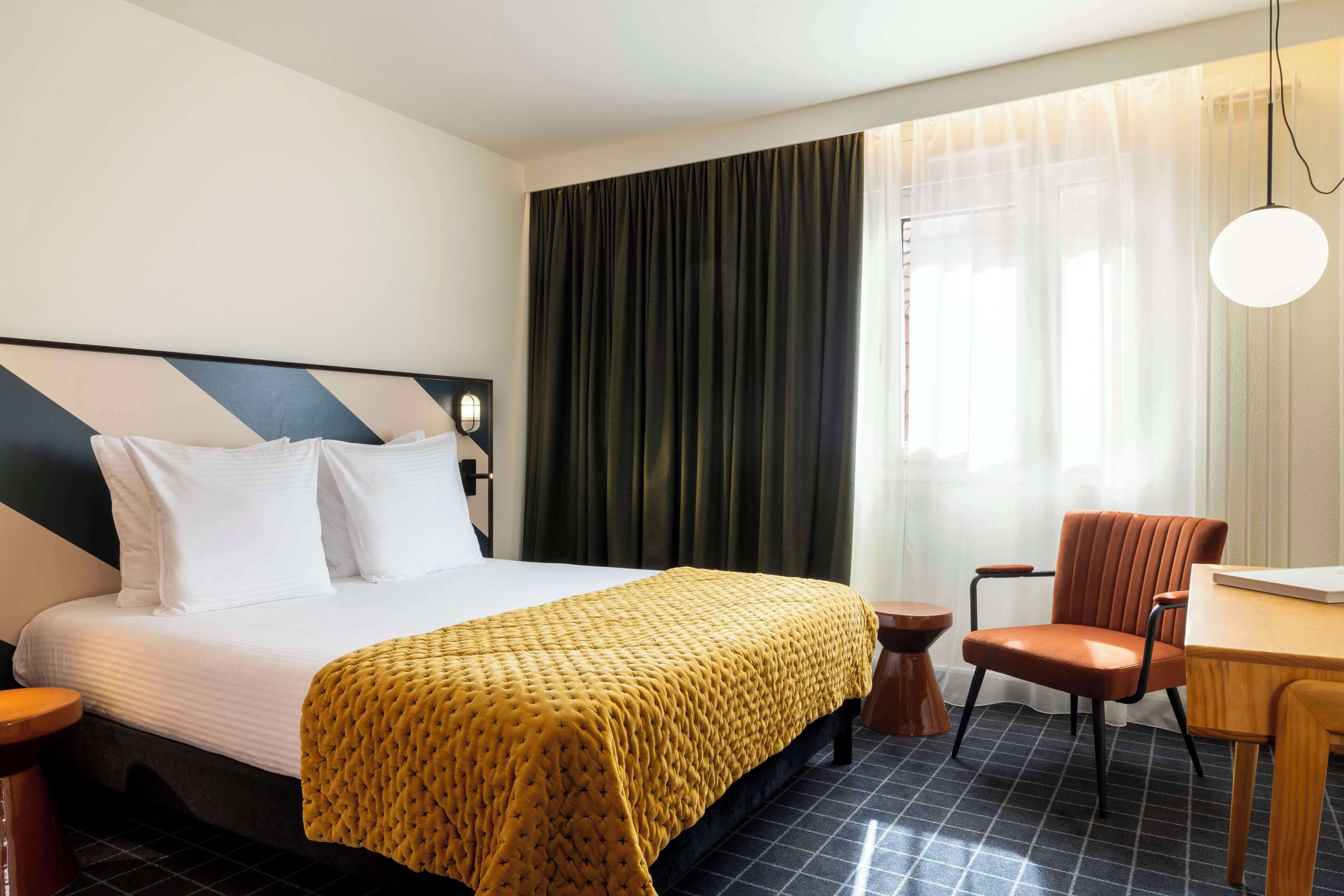Een hotelkamer met een bed, een stoel, een tafel en een raam met gordijnen.