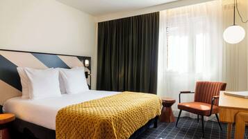 Een hotelkamer met een bed, een stoel, een tafel en een raam met gordijnen.