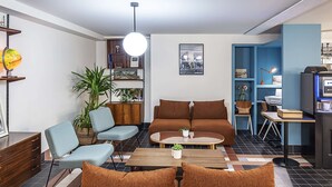 A modern living room with a brown sofa, blue armchairs, and a coffee table. There is a bookshelf with various items and a small desk with a computer. - Best Western Plus Hotel Cargo (Dunkirk)