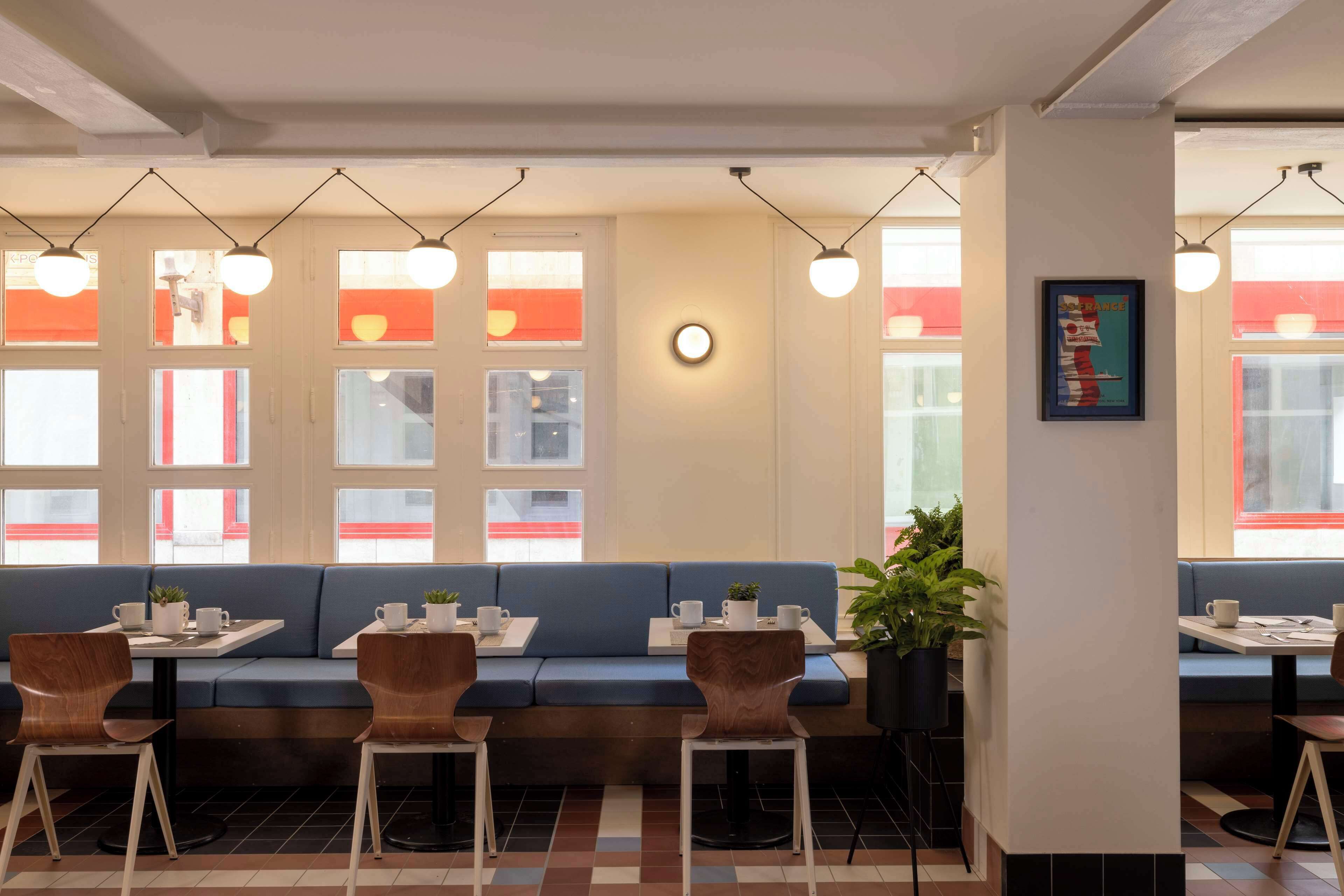 A modern interior with a blue sofa, wooden chairs, and tables, featuring pendant lighting and a clock on the wall.